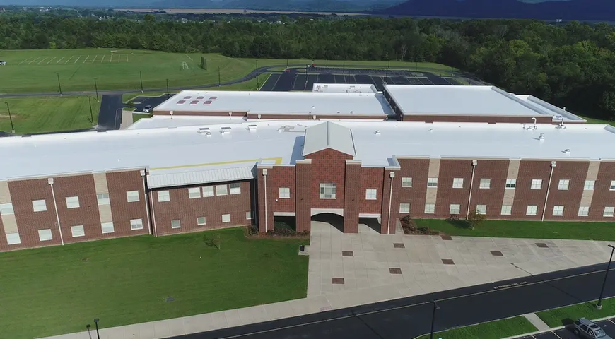 Aerial view of brick school with white roof restored with Tremco roofing’s weatherproofing materials. 